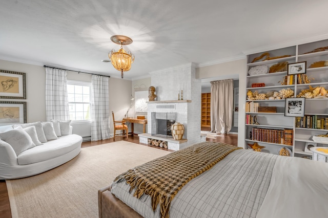 bedroom featuring a brick fireplace, wood finished floors, an inviting chandelier, and crown molding