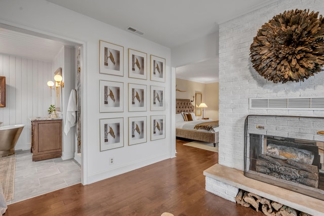 interior space featuring a brick fireplace, wood finished floors, visible vents, and baseboards