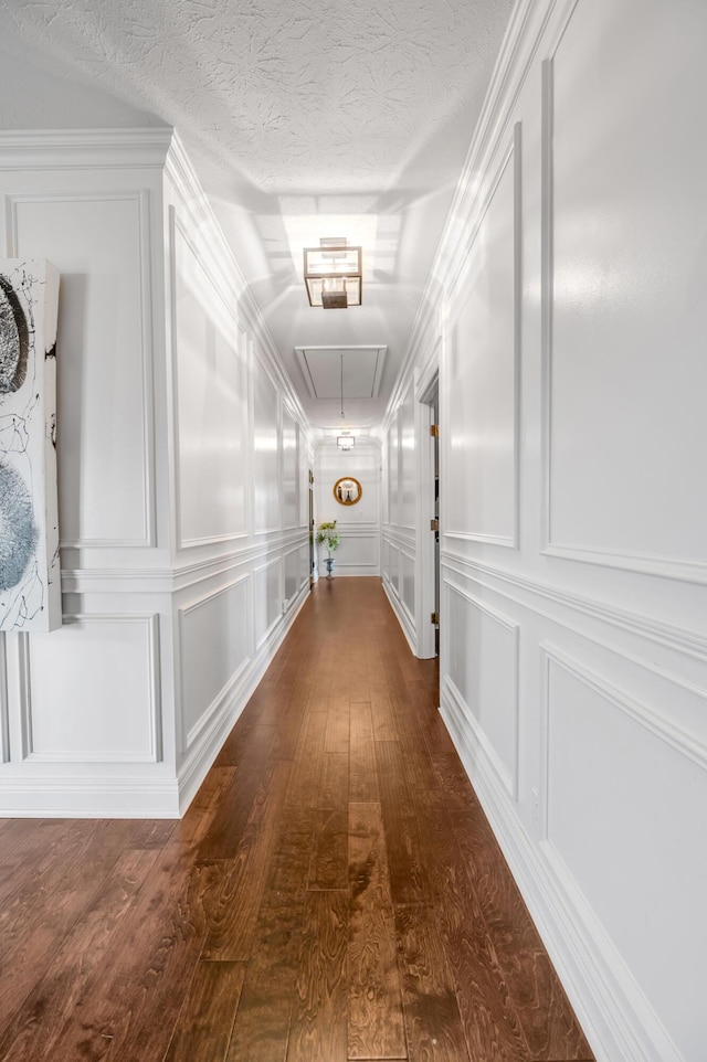 hall with a textured ceiling, dark wood-type flooring, attic access, and a decorative wall