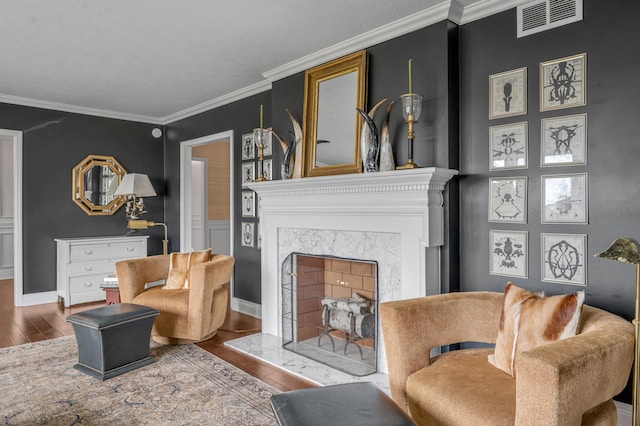 living room with baseboards, visible vents, ornamental molding, hardwood / wood-style floors, and a fireplace