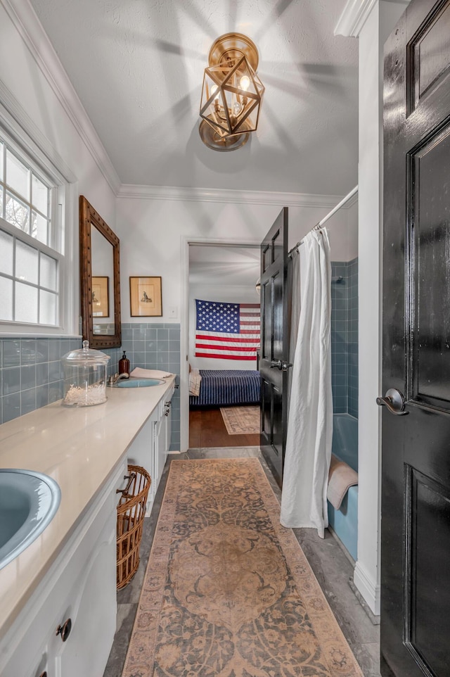 ensuite bathroom featuring double vanity, tile walls, ensuite bath, ornamental molding, and a sink