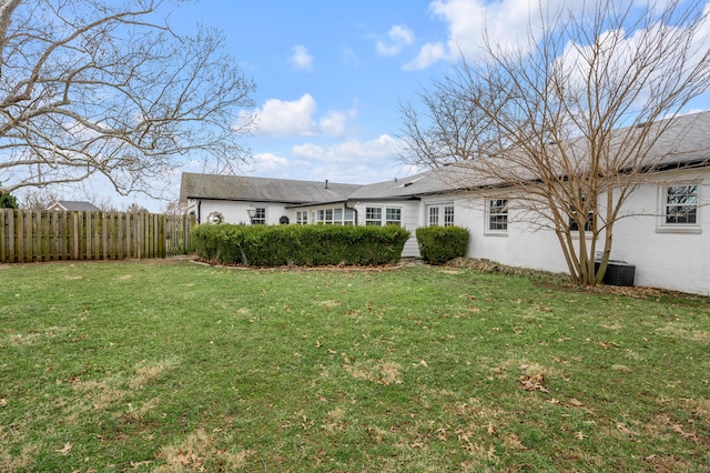 rear view of property featuring cooling unit, fence, and a lawn