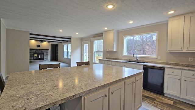 kitchen with sink, a center island, black dishwasher, white cabinets, and a stone fireplace