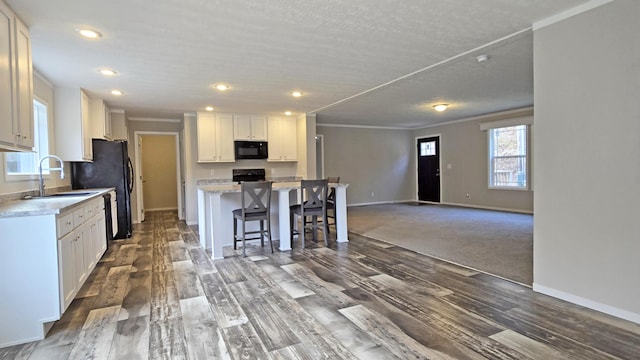 kitchen featuring sink, white cabinets, a kitchen bar, ornamental molding, and black appliances