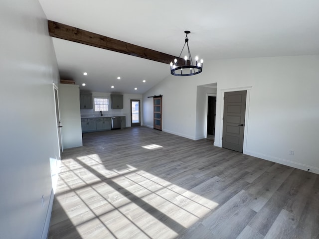 unfurnished living room with lofted ceiling with beams, a barn door, a chandelier, and light hardwood / wood-style floors