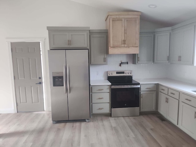 kitchen with stainless steel appliances, light wood-type flooring, light countertops, and lofted ceiling