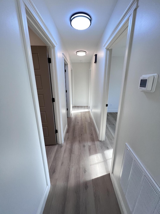 hall featuring visible vents, baseboards, and wood finished floors