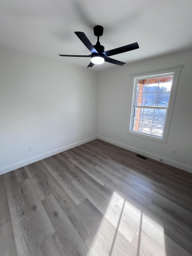 empty room featuring ceiling fan, wood finished floors, visible vents, and baseboards