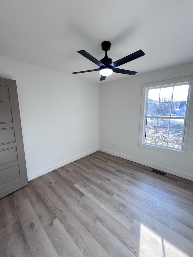 unfurnished room with ceiling fan, wood finished floors, visible vents, and baseboards