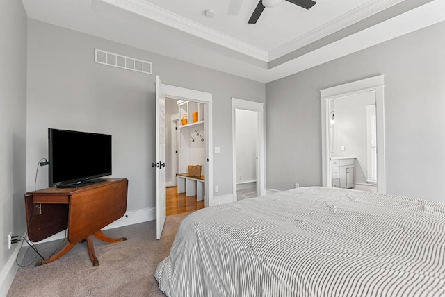 carpeted bedroom with a raised ceiling, ornamental molding, ensuite bathroom, and ceiling fan