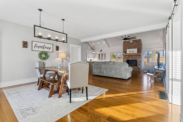 dining space with vaulted ceiling with beams, ceiling fan with notable chandelier, hardwood / wood-style floors, and a barn door