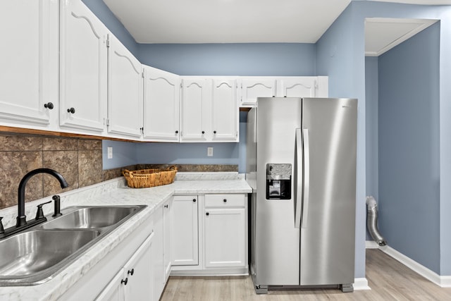 kitchen with sink, white cabinetry, stainless steel fridge, light hardwood / wood-style floors, and backsplash