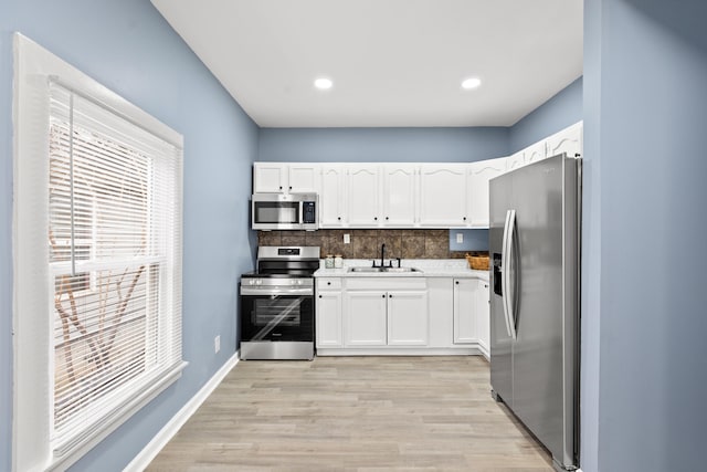 kitchen with sink, white cabinets, backsplash, stainless steel appliances, and light hardwood / wood-style flooring