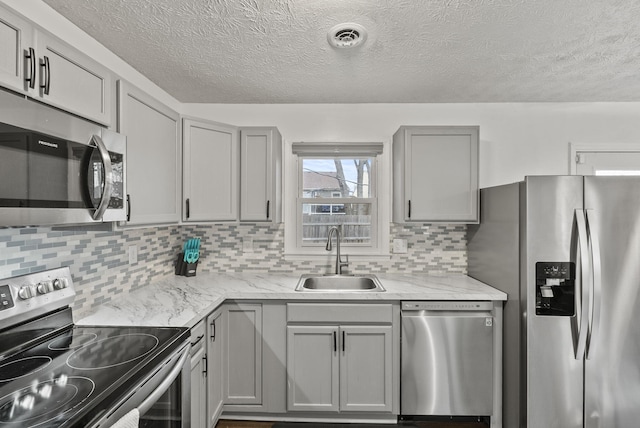 kitchen with sink, appliances with stainless steel finishes, gray cabinetry, light stone counters, and decorative backsplash