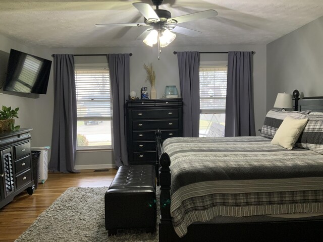 bedroom with ceiling fan, wood-type flooring, and a textured ceiling