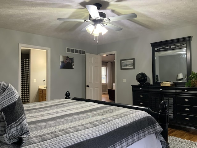 bedroom with wood finished floors, visible vents, ceiling fan, a textured ceiling, and connected bathroom