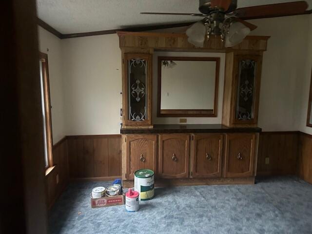 unfurnished dining area featuring wood walls, crown molding, a textured ceiling, carpet floors, and ceiling fan