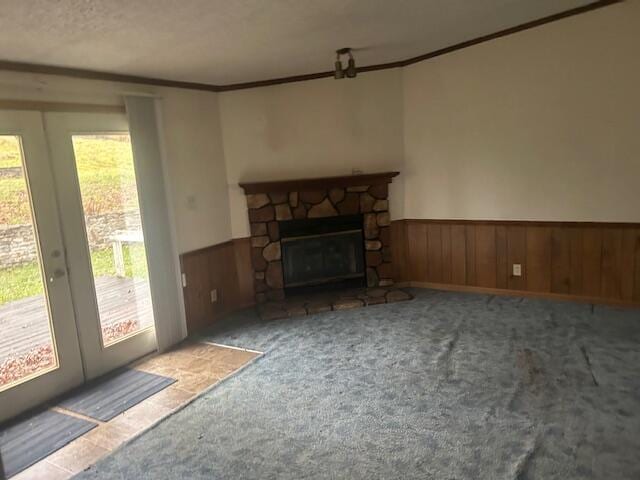 unfurnished living room featuring crown molding, a stone fireplace, a wealth of natural light, and carpet flooring