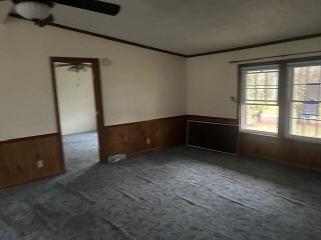 carpeted empty room with wooden walls, ornamental molding, and vaulted ceiling