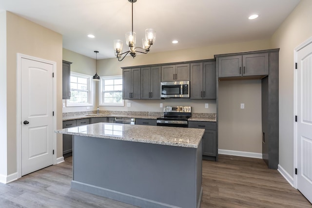 kitchen with decorative light fixtures, a kitchen island, stainless steel appliances, light stone countertops, and light hardwood / wood-style floors