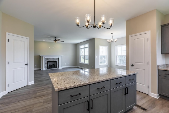 kitchen with gray cabinetry, a kitchen island, pendant lighting, a high end fireplace, and light stone countertops