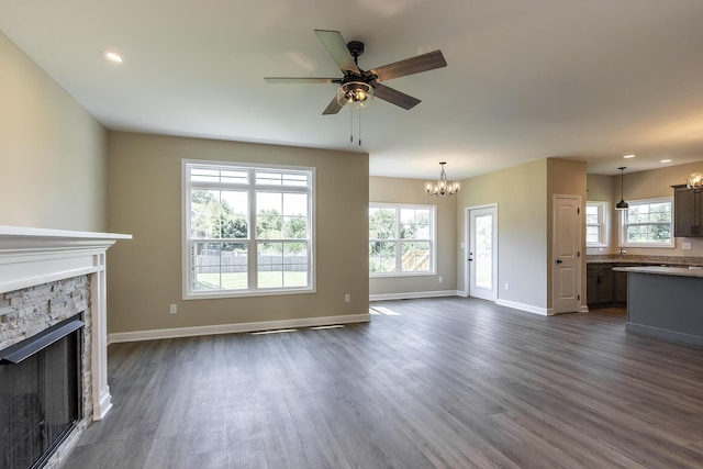 unfurnished living room featuring a stone fireplace, a wealth of natural light, and dark wood-type flooring