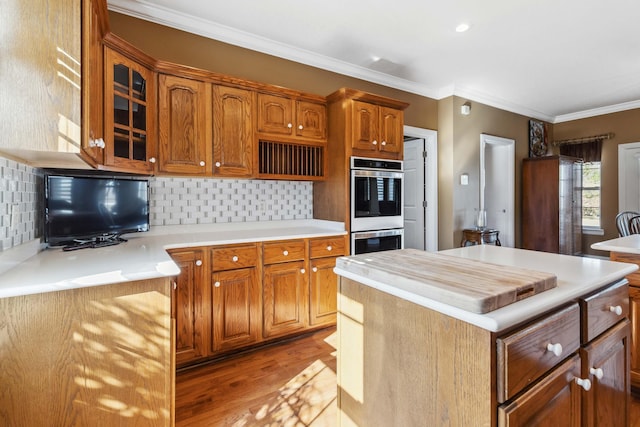 kitchen with light hardwood / wood-style flooring, double oven, backsplash, a center island, and ornamental molding