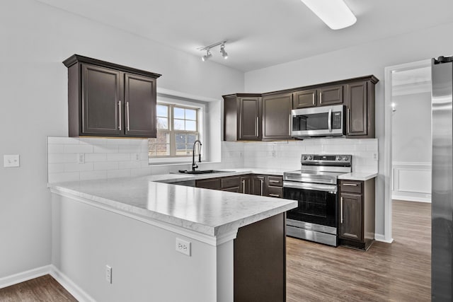 kitchen with a peninsula, appliances with stainless steel finishes, light countertops, and a sink