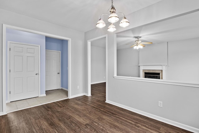 interior space featuring a fireplace, baseboards, wood finished floors, and ceiling fan with notable chandelier