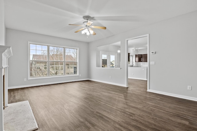 unfurnished living room featuring a fireplace with flush hearth, dark wood finished floors, baseboards, and ceiling fan