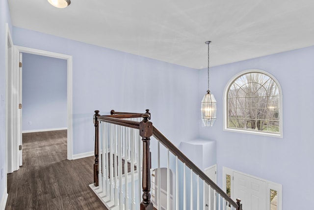 hall featuring baseboards, dark wood-style flooring, an upstairs landing, and an inviting chandelier