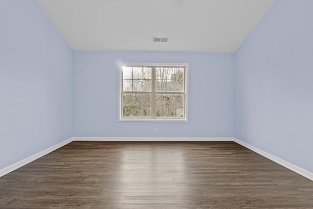 empty room featuring dark wood-style flooring, visible vents, and baseboards