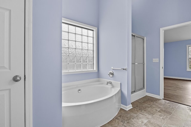 bathroom featuring a garden tub, a shower stall, and baseboards