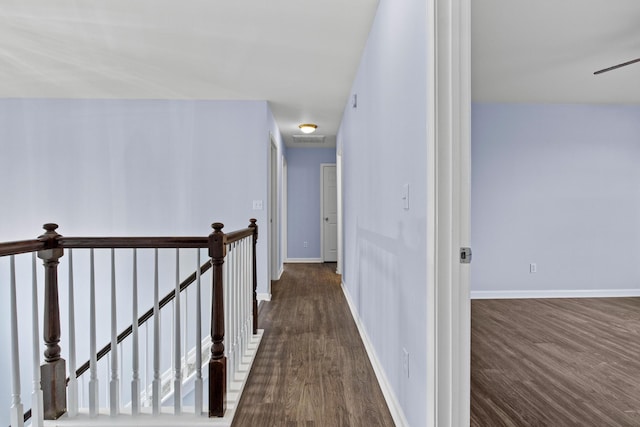 hallway with baseboards, dark wood finished floors, and an upstairs landing