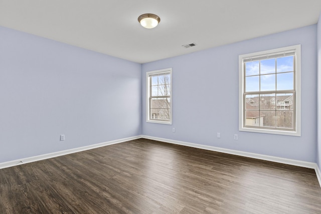 spare room featuring visible vents, baseboards, and dark wood-type flooring