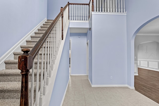 stairs featuring baseboards, arched walkways, ornamental molding, tile patterned floors, and a high ceiling