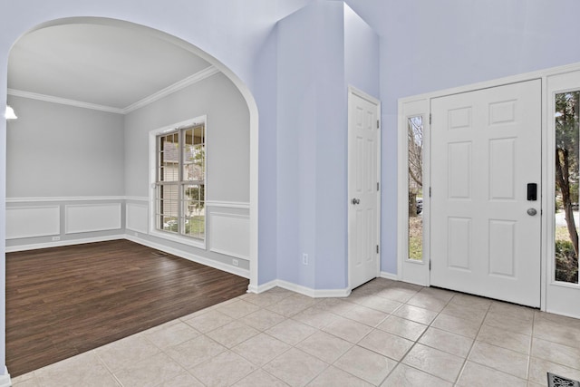 entrance foyer featuring visible vents, crown molding, a decorative wall, and light tile patterned floors