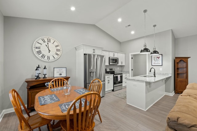 dining room featuring vaulted ceiling, sink, and light hardwood / wood-style flooring