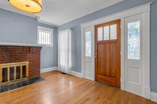 foyer with crown molding, a brick fireplace, and wood-type flooring