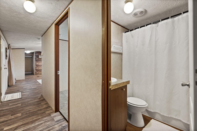 bathroom featuring wood-type flooring, vanity, toilet, a textured ceiling, and a shower with curtain