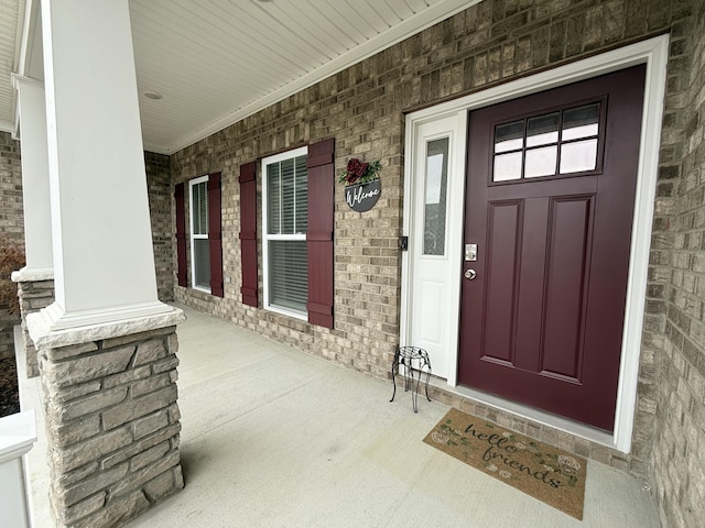 entrance to property featuring a porch and brick siding