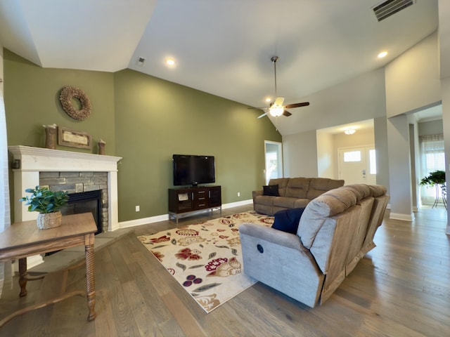 living room featuring visible vents, vaulted ceiling, a stone fireplace, wood finished floors, and a ceiling fan