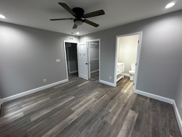 unfurnished bedroom with dark wood-type flooring, a walk in closet, ensuite bath, a closet, and ceiling fan