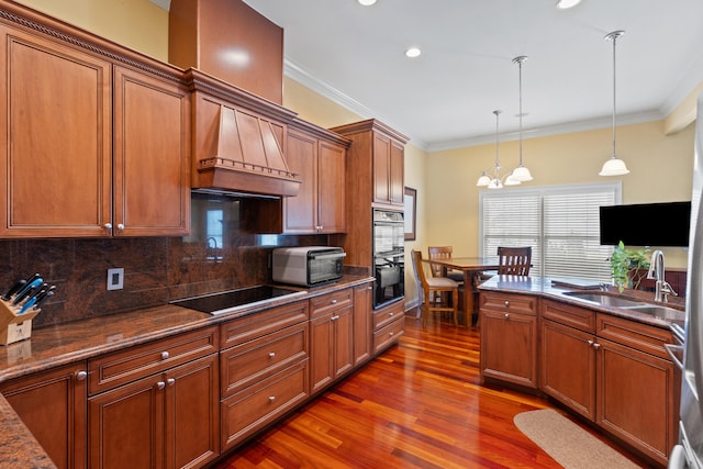 kitchen with black appliances, crown molding, brown cabinetry, and a sink