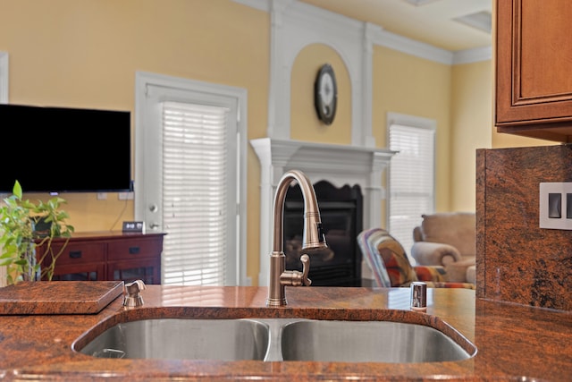 kitchen featuring a fireplace, dark stone counters, brown cabinetry, and a sink