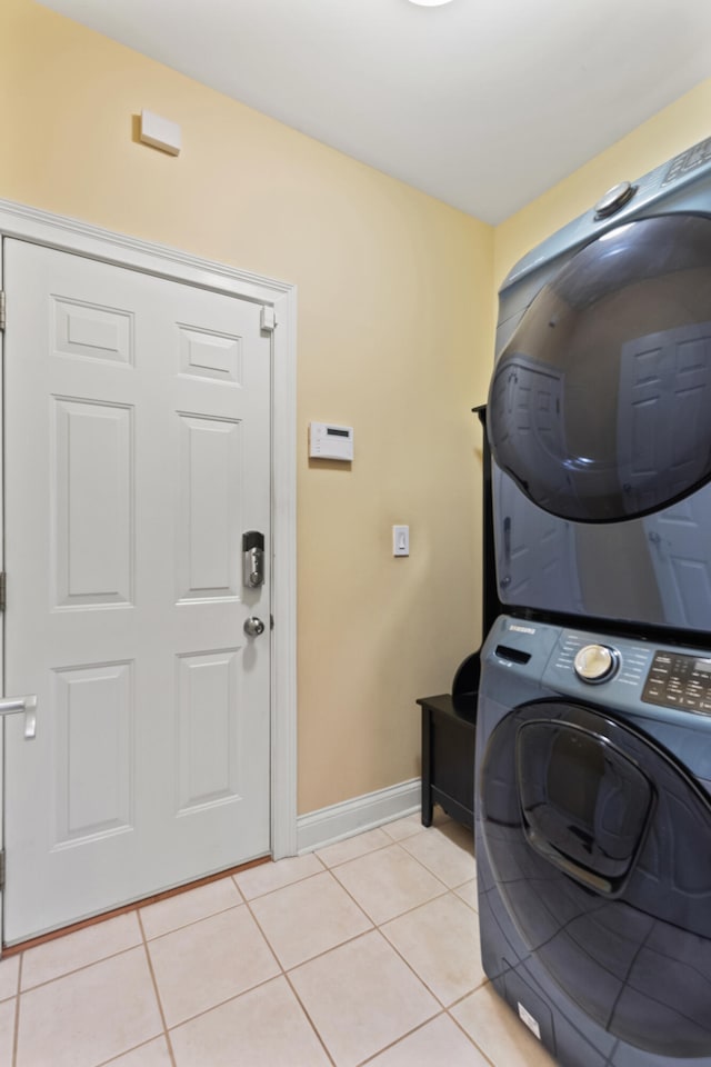 laundry area with light tile patterned floors, laundry area, stacked washer / dryer, and baseboards