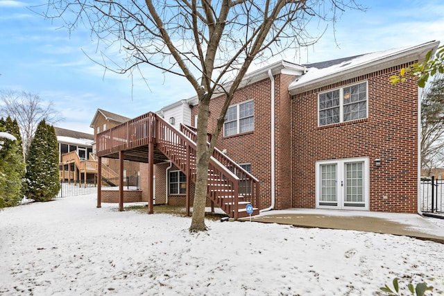 snow covered property with french doors, stairs, fence, a wooden deck, and brick siding