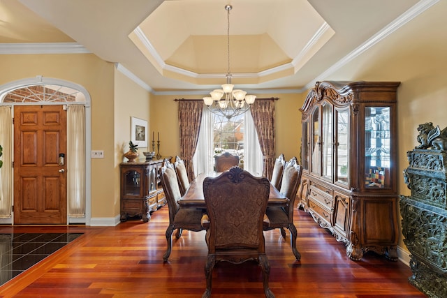 dining space with dark wood-type flooring, a raised ceiling, a notable chandelier, and ornamental molding