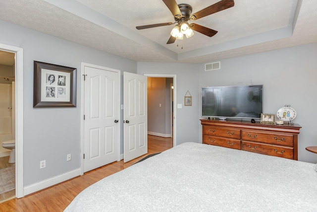 bedroom with connected bathroom, a raised ceiling, light hardwood / wood-style floors, and a textured ceiling