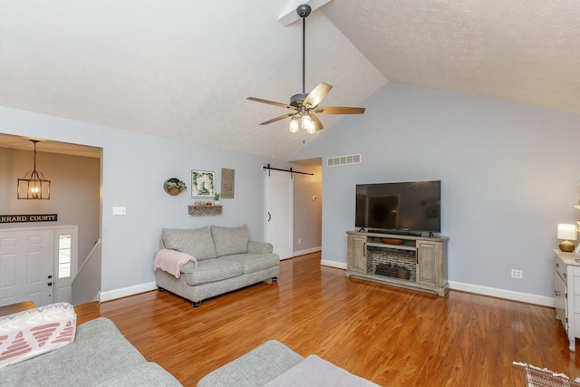 living room featuring ceiling fan, a barn door, a textured ceiling, and light hardwood / wood-style floors